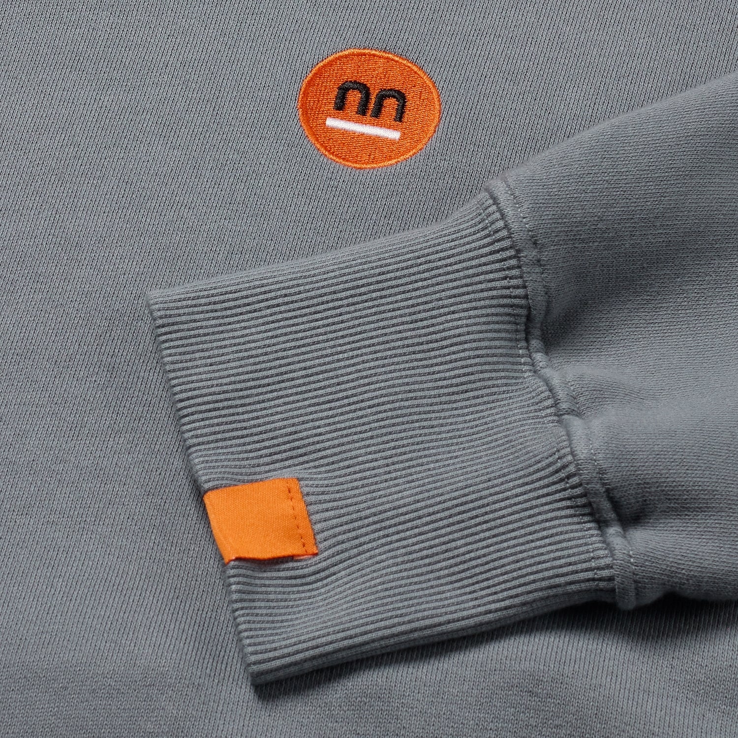 Close-up of grey hoodie cuff and logo, detailed craftsmanship.