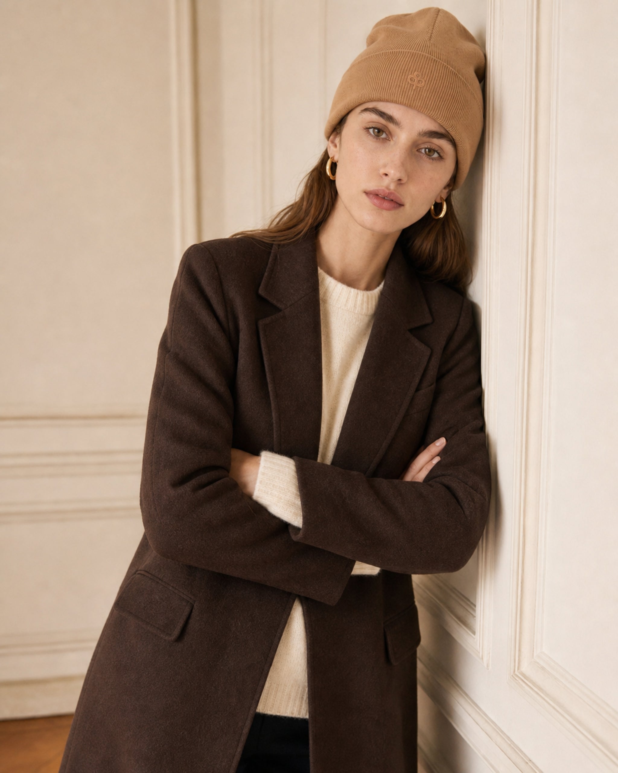Woman in a camel ribbed beanie and brown wool coat, arms crossed