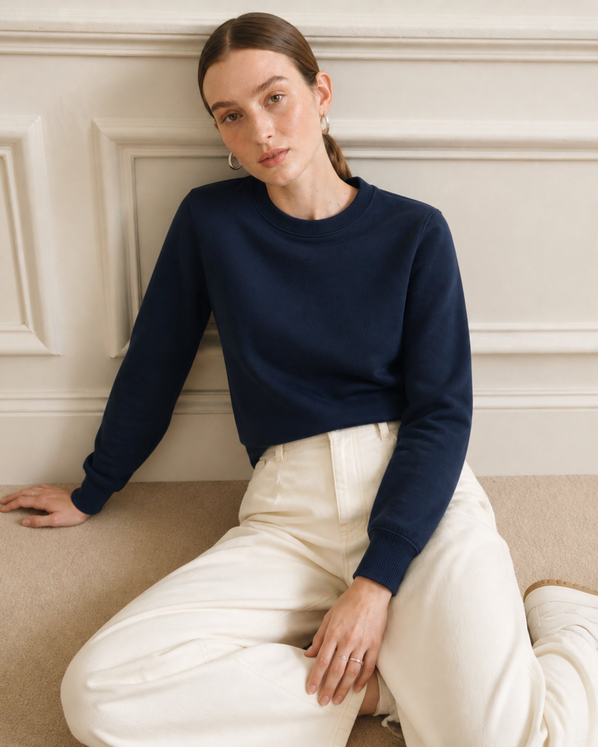 Woman in a navy cotton sweatshirt and cream trousers seated on a sofa